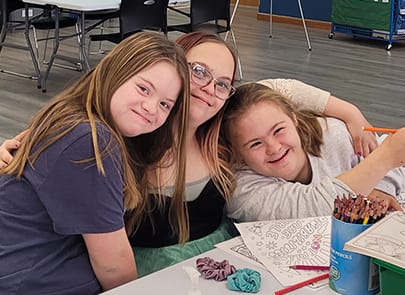 Three young girls hugging in classroom