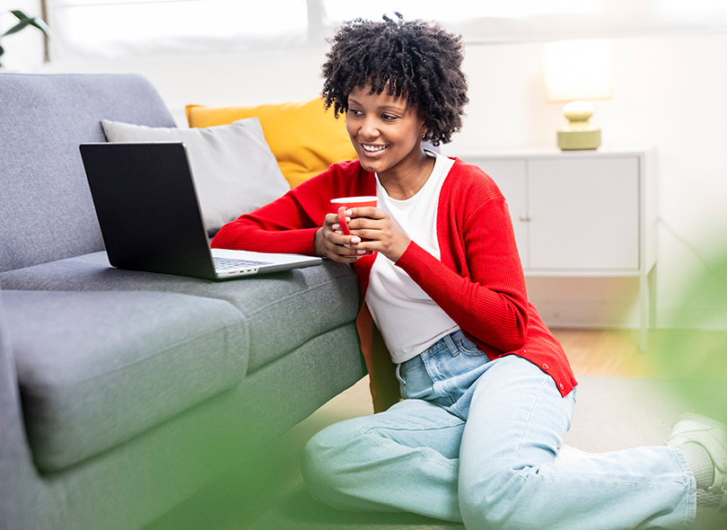 Woman sitting on ground in front of laptop with coffee 
