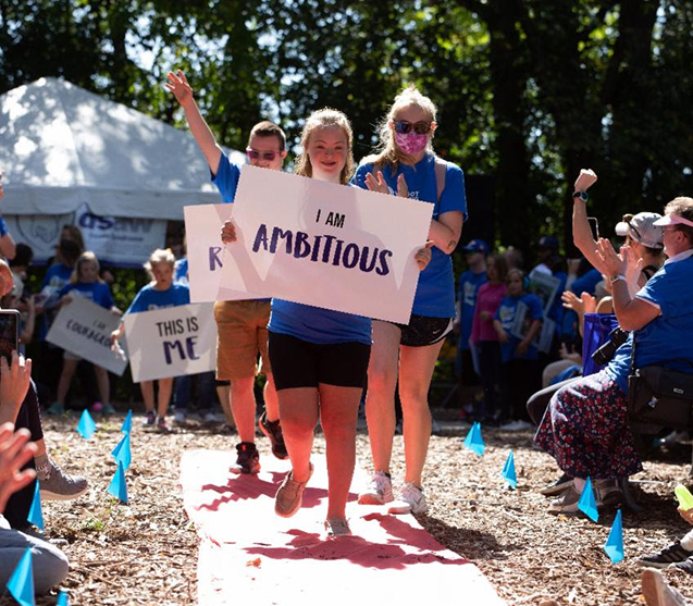 Photo of young child in a parade holding a sign that says I Am Ambitious