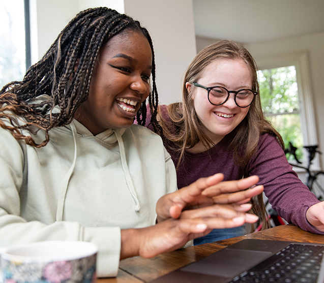 Two girls smiling and laughing at computer screen 